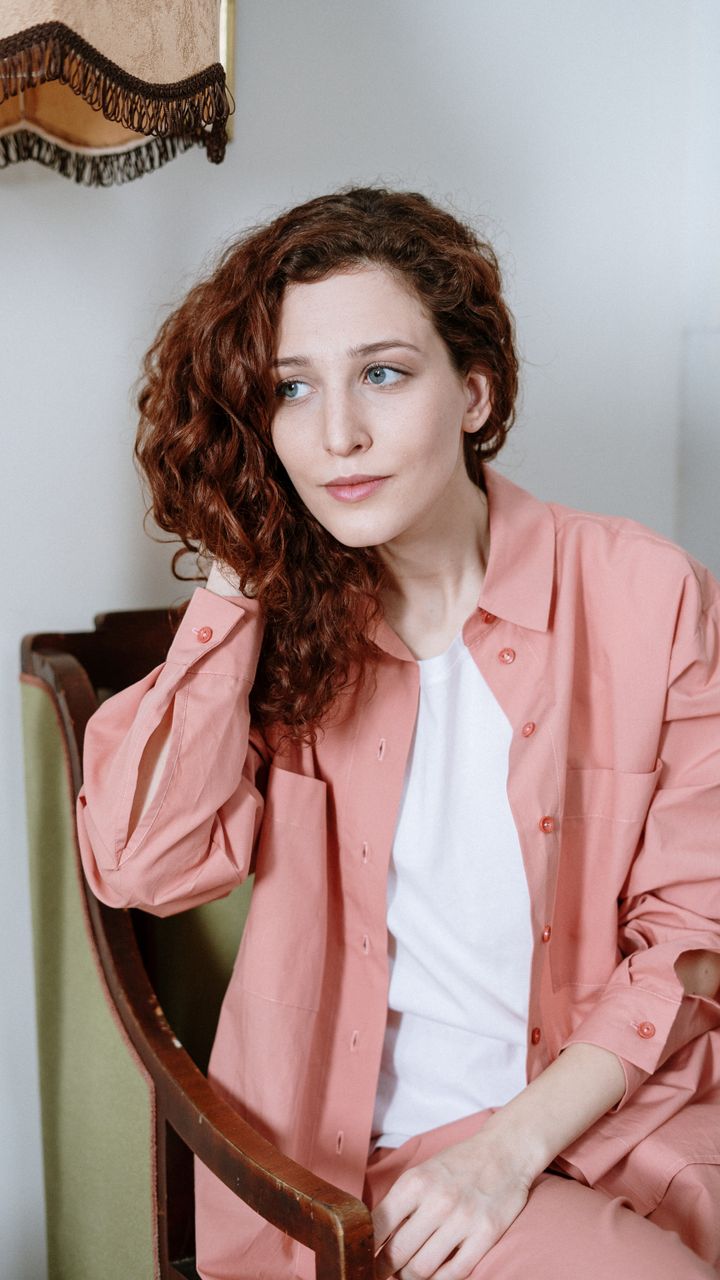 Red-haired woman seated indoors in a coral shirt
